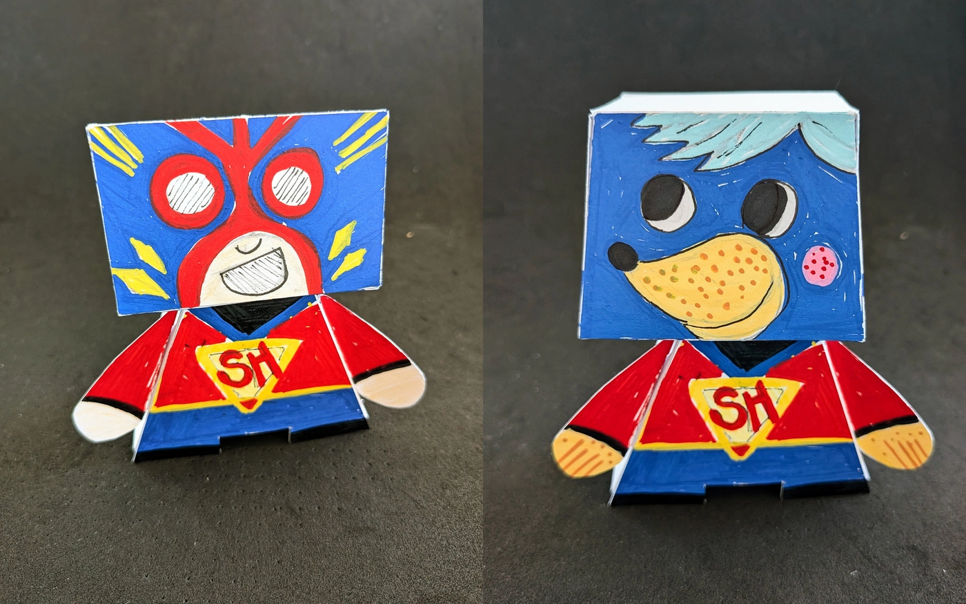 Hero or Villain? — two hand-painted paper toys: a masked hero and a blue bear character, both with an "SH" emblem