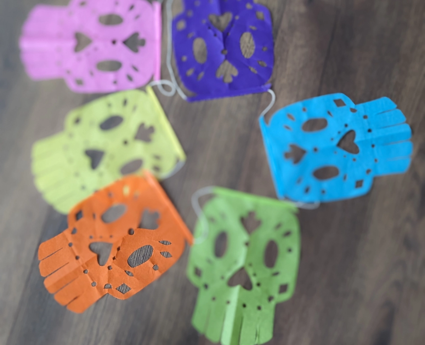 Six papel picado calaveras hand-cut from light crepe paper in pink, purple, yellow, blue, orange, and green