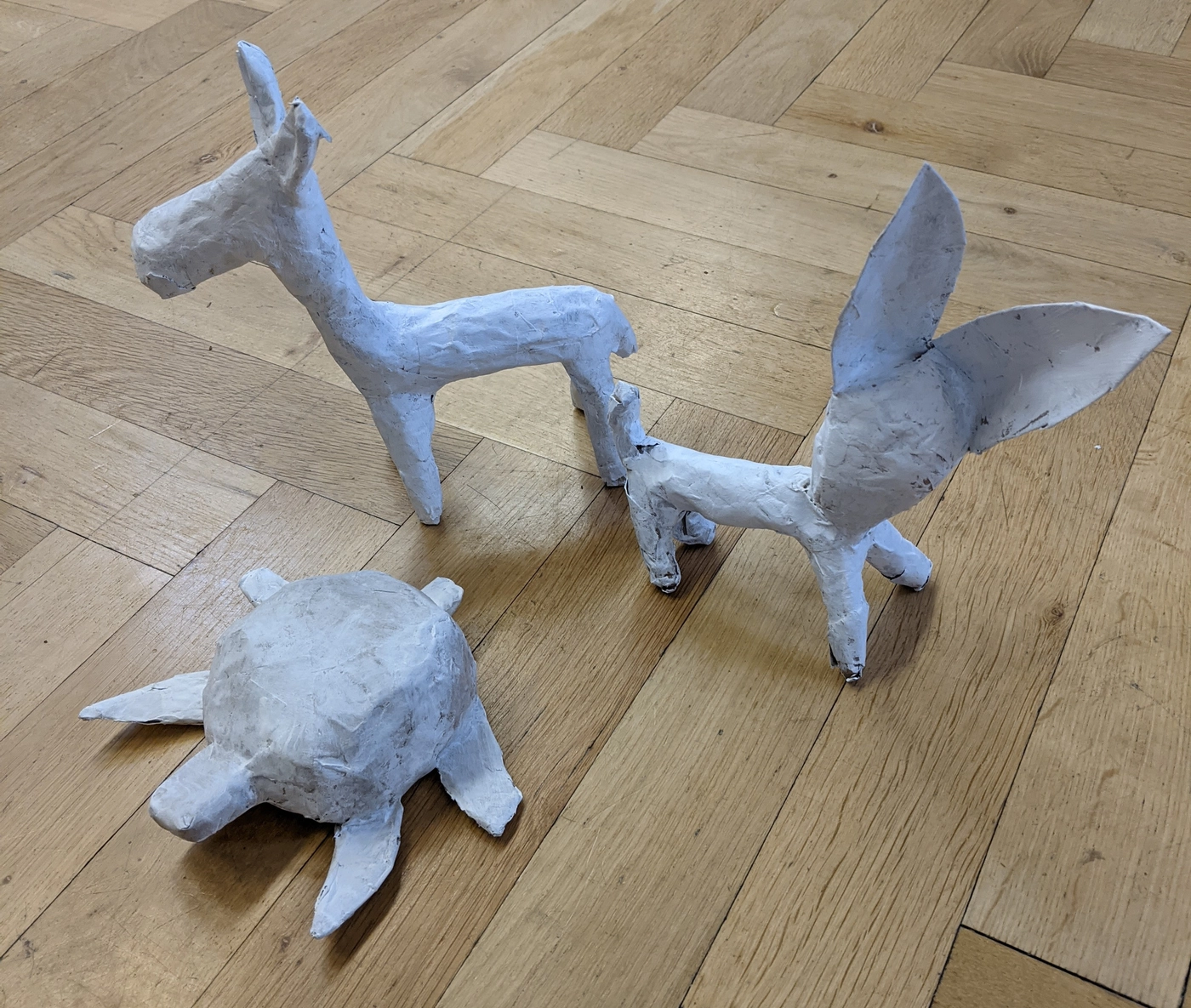 Three cartonería animals in white paper on the parquet, dried overnight and waiting for their paint