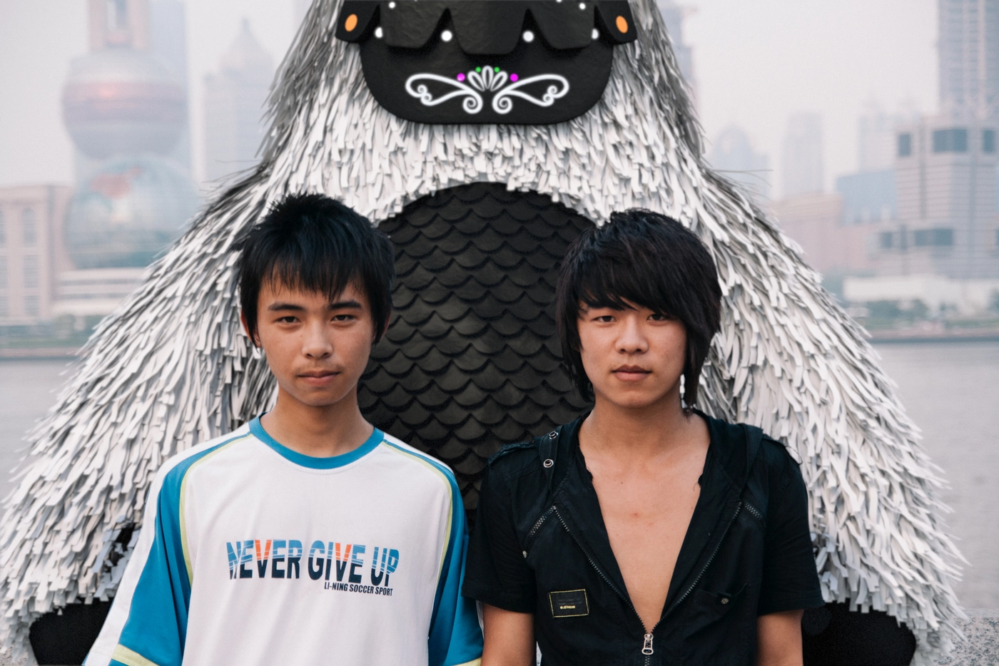 A sidewalk along the river in Shanghai. Two young men posed for their own photograph nearby, neither one looking his way.